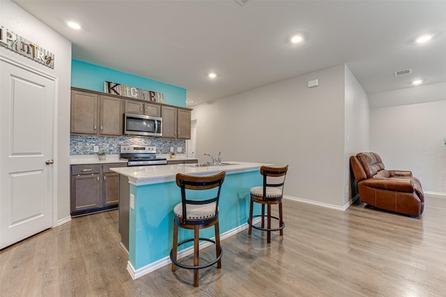 kitchen featuring stainless steel appliances, backsplash, a breakfast bar area, a center island with sink, and light wood-type flooring