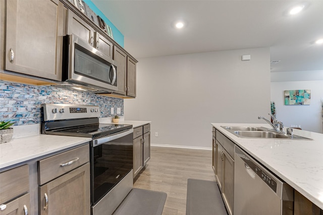 kitchen featuring sink, light hardwood / wood-style flooring, appliances with stainless steel finishes, tasteful backsplash, and light stone counters