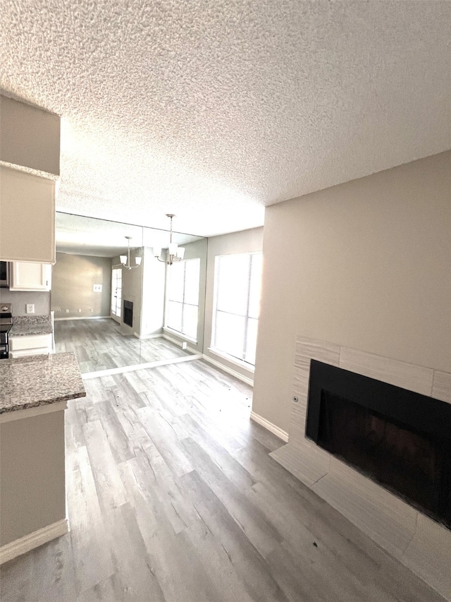 unfurnished living room with a notable chandelier, light wood-type flooring, and a textured ceiling