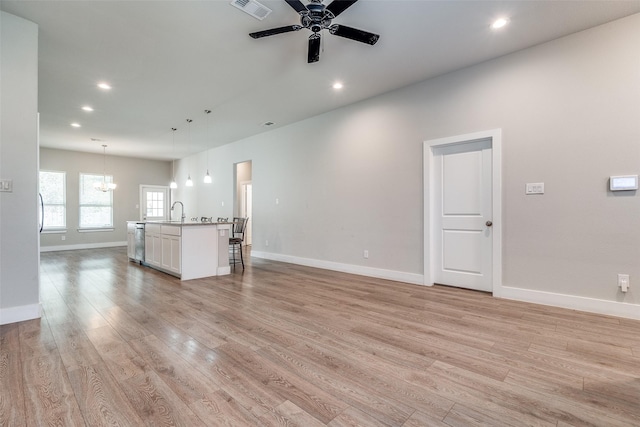 unfurnished living room with ceiling fan with notable chandelier, light hardwood / wood-style floors, and sink