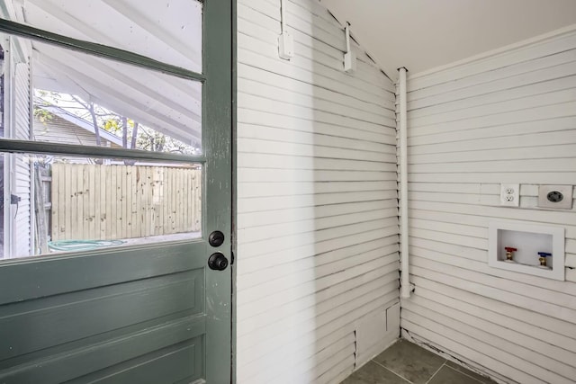 interior space with electric dryer hookup, wooden walls, dark tile patterned floors, and washer hookup