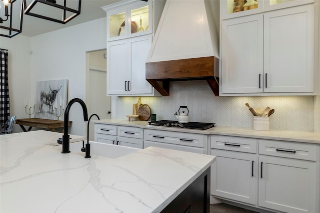 kitchen featuring custom exhaust hood, white cabinets, tasteful backsplash, light stone counters, and stainless steel gas cooktop