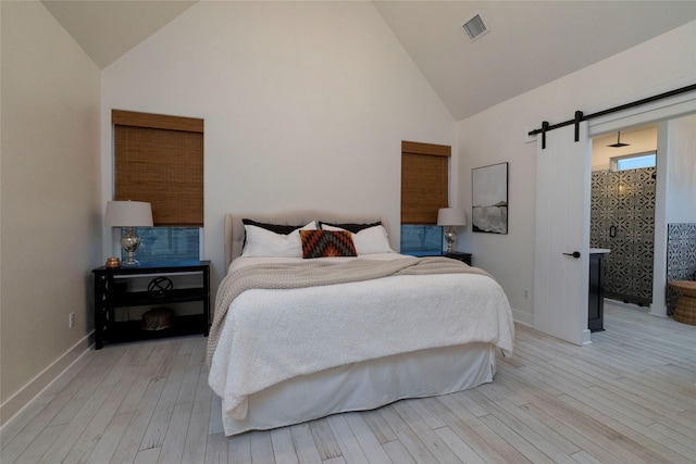 bedroom featuring a barn door, high vaulted ceiling, and light hardwood / wood-style flooring