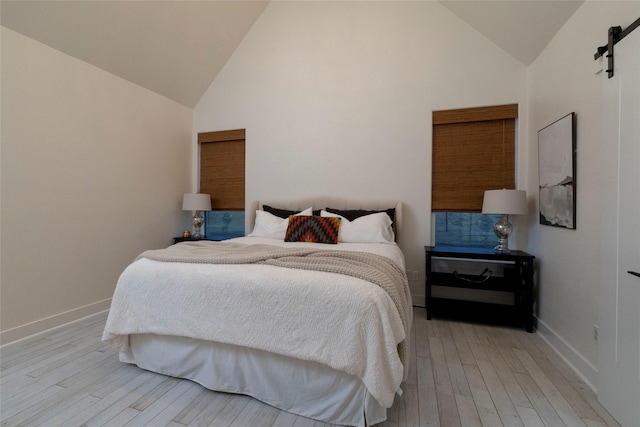 bedroom with a barn door, light wood-type flooring, and high vaulted ceiling