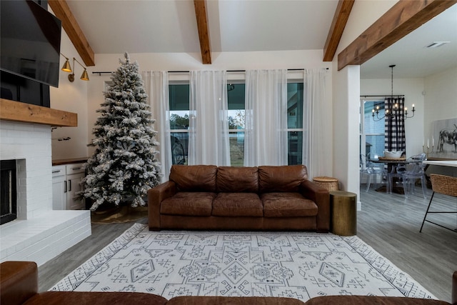 living room with beam ceiling, a brick fireplace, a chandelier, and light wood-type flooring