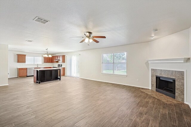 unfurnished living room featuring a tile fireplace, sink, hardwood / wood-style flooring, ceiling fan, and a textured ceiling