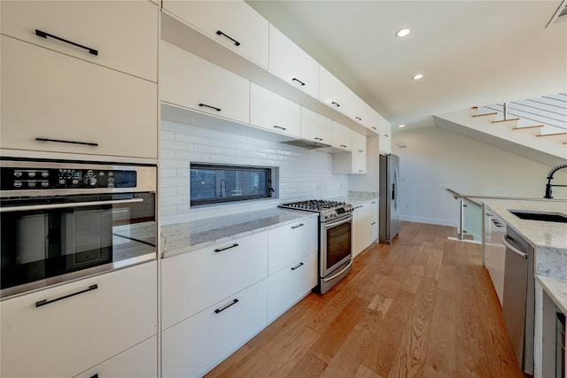 kitchen featuring light stone countertops, sink, appliances with stainless steel finishes, white cabinets, and light wood-type flooring