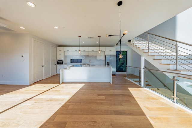 kitchen with a center island with sink, hanging light fixtures, light wood-type flooring, appliances with stainless steel finishes, and white cabinetry