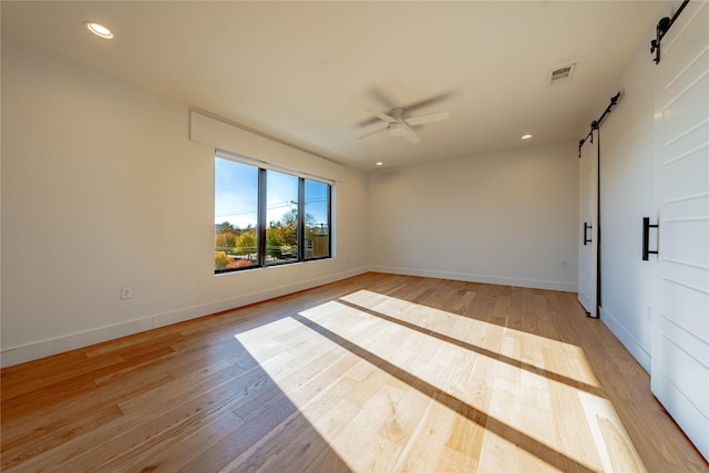 unfurnished room featuring a barn door, light hardwood / wood-style floors, and ceiling fan