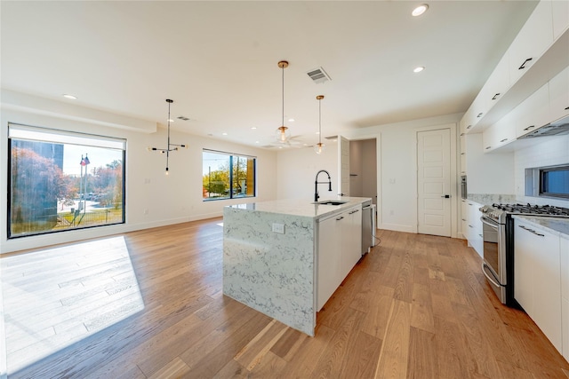 kitchen featuring white cabinets, light hardwood / wood-style floors, hanging light fixtures, and appliances with stainless steel finishes