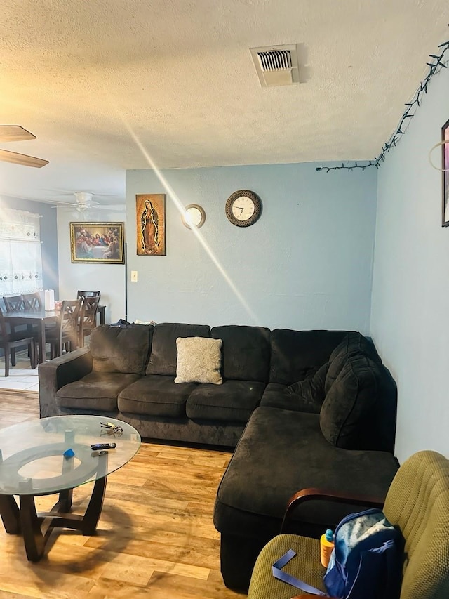 living room with ceiling fan, light wood-type flooring, and a textured ceiling