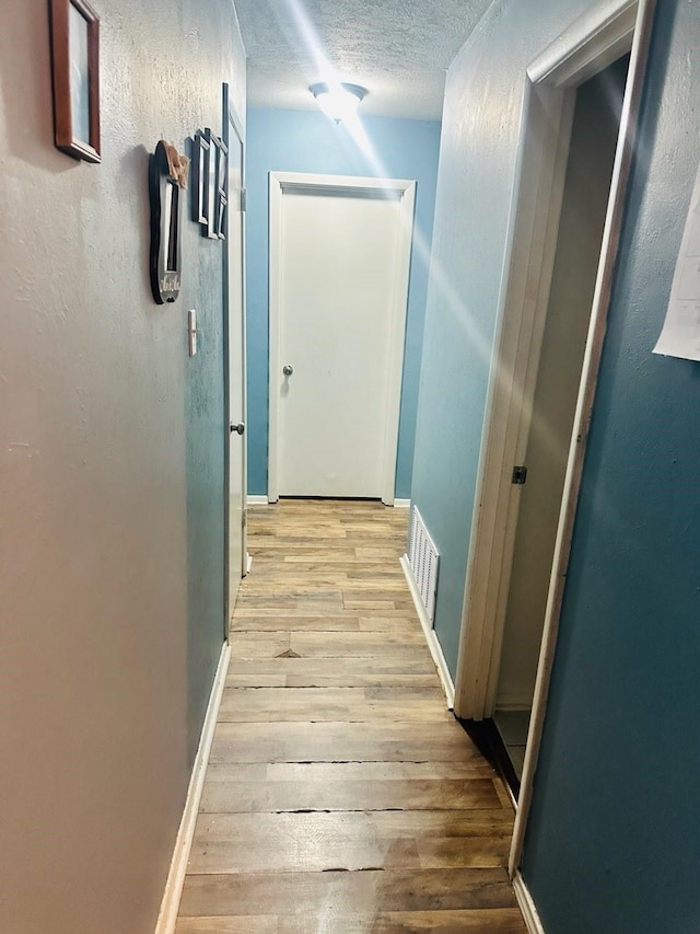 hall featuring a textured ceiling and light hardwood / wood-style flooring