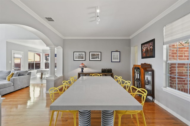 dining room with light hardwood / wood-style flooring, crown molding, and ornate columns