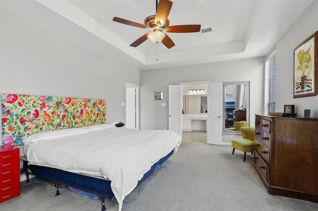 bedroom featuring a raised ceiling, ensuite bath, ceiling fan, and light colored carpet