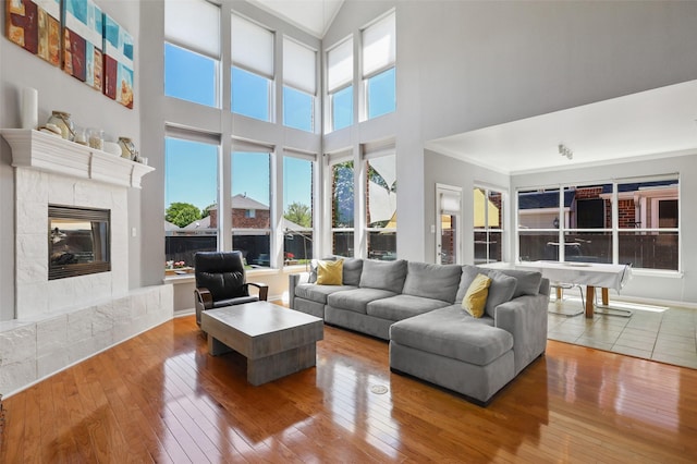 living room featuring a tile fireplace, a high ceiling, hardwood / wood-style flooring, and ornamental molding