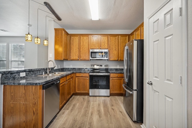 kitchen with sink, dark stone countertops, appliances with stainless steel finishes, decorative light fixtures, and light hardwood / wood-style floors