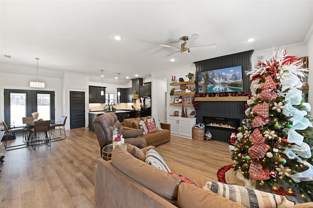 living room featuring ceiling fan, a fireplace, light hardwood / wood-style floors, and ornamental molding