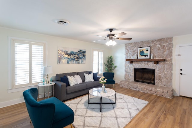 living room with hardwood / wood-style flooring, ceiling fan, a stone fireplace, and crown molding