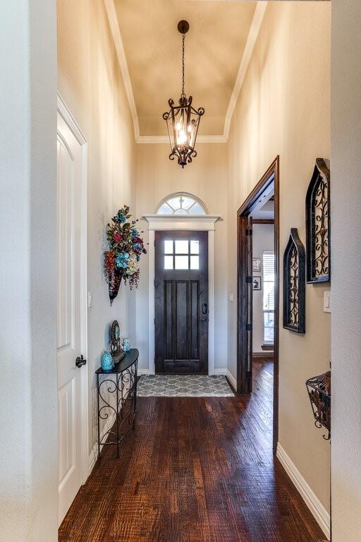 entryway featuring an inviting chandelier, baseboards, crown molding, and wood finished floors