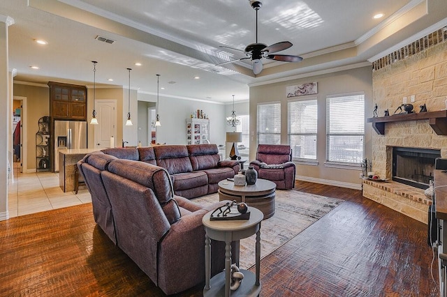 living room featuring hardwood / wood-style floors, a fireplace, ceiling fan, a tray ceiling, and crown molding