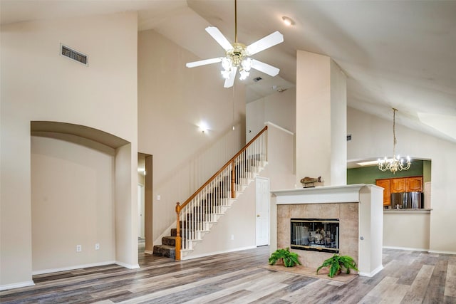 unfurnished living room with ceiling fan with notable chandelier, a tile fireplace, wood-type flooring, and high vaulted ceiling