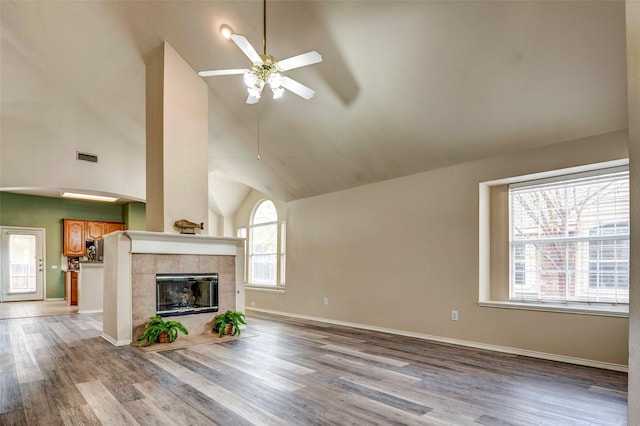 unfurnished living room featuring a tiled fireplace, ceiling fan, light hardwood / wood-style flooring, and high vaulted ceiling