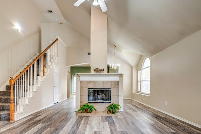 unfurnished living room with a tiled fireplace, hardwood / wood-style floors, high vaulted ceiling, and ceiling fan with notable chandelier