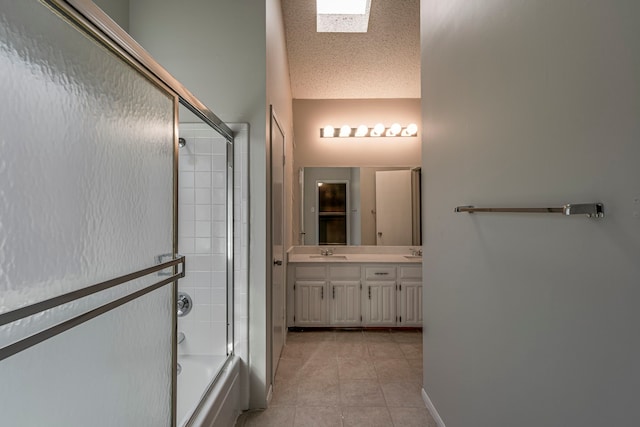 bathroom with a skylight, tile patterned floors, bath / shower combo with glass door, a textured ceiling, and vanity