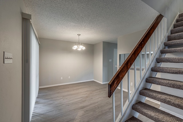 staircase with a textured ceiling, a notable chandelier, and hardwood / wood-style flooring