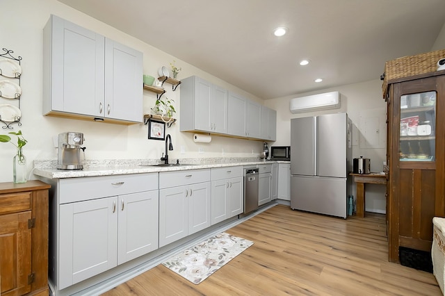 kitchen with sink, a wall mounted AC, refrigerator, light wood-type flooring, and white cabinets