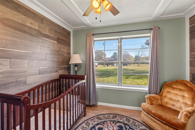 bedroom featuring a crib, light wood-type flooring, ceiling fan, and wood walls