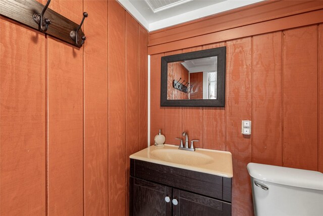 bathroom featuring vanity, wood walls, and toilet