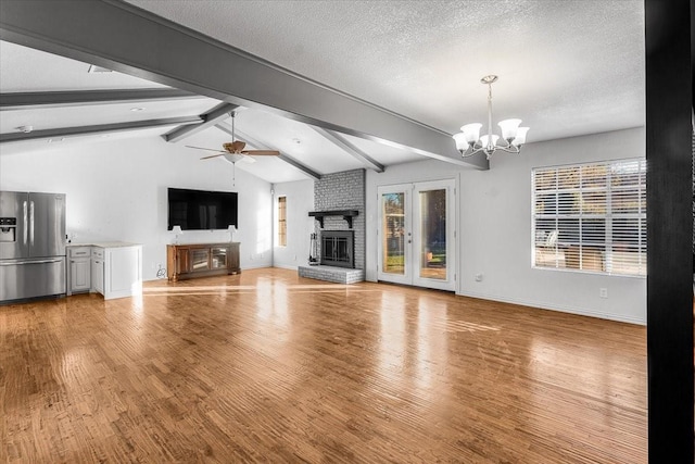 unfurnished living room featuring vaulted ceiling with beams, light wood-type flooring, a fireplace, and ceiling fan with notable chandelier