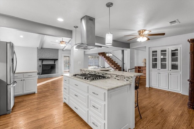 kitchen featuring hanging light fixtures, stainless steel appliances, island exhaust hood, light hardwood / wood-style floors, and white cabinets