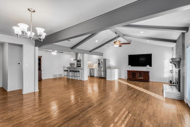 unfurnished living room with vaulted ceiling with beams, a textured ceiling, a fireplace, ceiling fan with notable chandelier, and hardwood / wood-style flooring