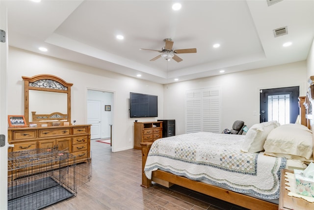 bedroom with hardwood / wood-style floors, ceiling fan, and a tray ceiling