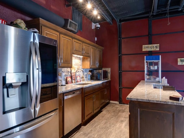 kitchen featuring light stone countertops, light wood-type flooring, backsplash, stainless steel appliances, and sink