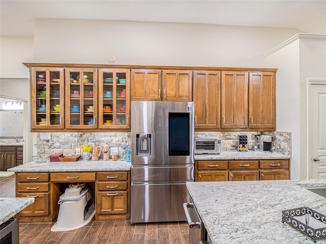 kitchen featuring stainless steel refrigerator with ice dispenser, backsplash, light stone counters, dark wood-type flooring, and sink