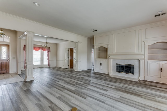 unfurnished living room with a tile fireplace, crown molding, light hardwood / wood-style flooring, and a notable chandelier