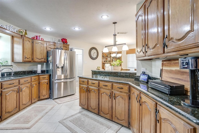 kitchen with sink, stainless steel fridge, dark stone countertops, light tile patterned floors, and decorative light fixtures