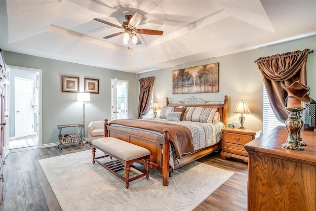 bedroom featuring ensuite bath, a tray ceiling, ceiling fan, wood-type flooring, and multiple windows