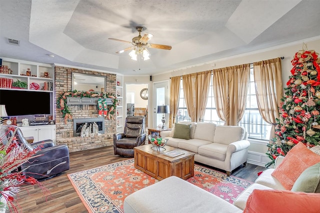 living room with hardwood / wood-style floors, ceiling fan, a fireplace, a textured ceiling, and a tray ceiling