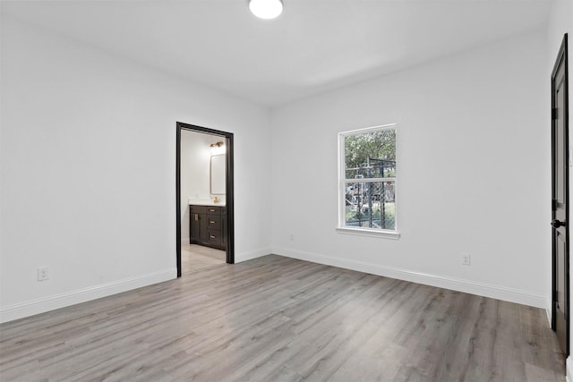 unfurnished bedroom with ensuite bathroom and light wood-type flooring