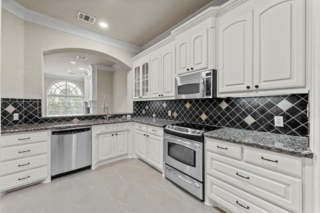 kitchen with appliances with stainless steel finishes, dark stone counters, crown molding, sink, and white cabinetry