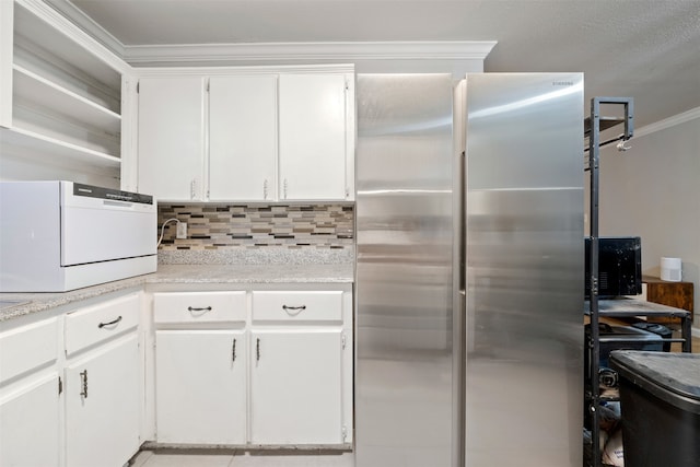 kitchen featuring white cabinets, decorative backsplash, stainless steel refrigerator, and ornamental molding