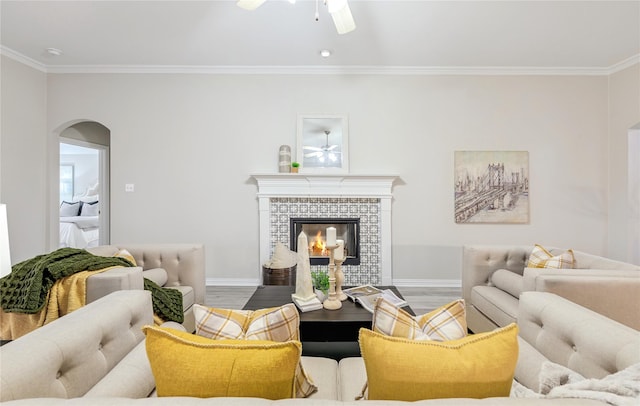 living room with hardwood / wood-style flooring, ceiling fan, ornamental molding, and a fireplace