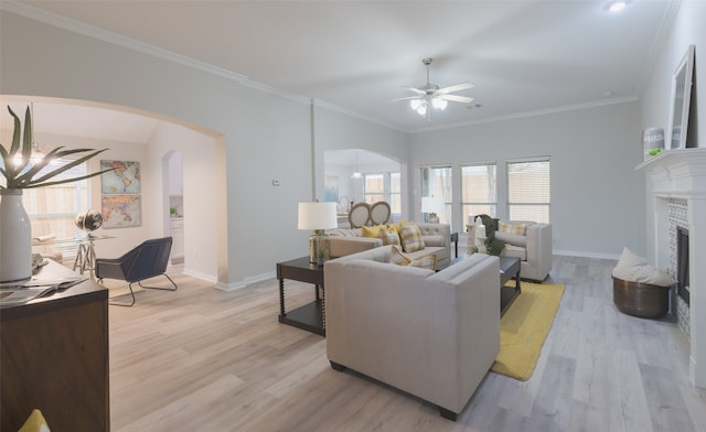 living room with ceiling fan with notable chandelier, light wood-type flooring, crown molding, and a tiled fireplace