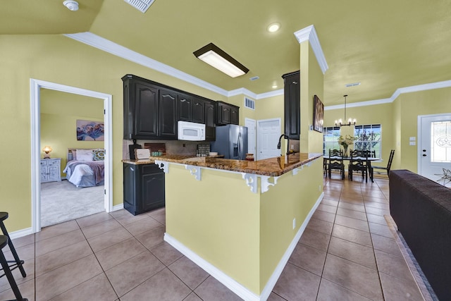 kitchen with a breakfast bar area, stainless steel fridge, dark stone counters, and ornamental molding