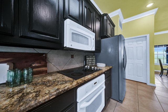 kitchen featuring tasteful backsplash, dark stone counters, light tile patterned floors, crown molding, and white appliances