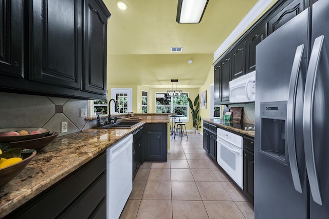 kitchen featuring pendant lighting, white appliances, backsplash, sink, and a notable chandelier